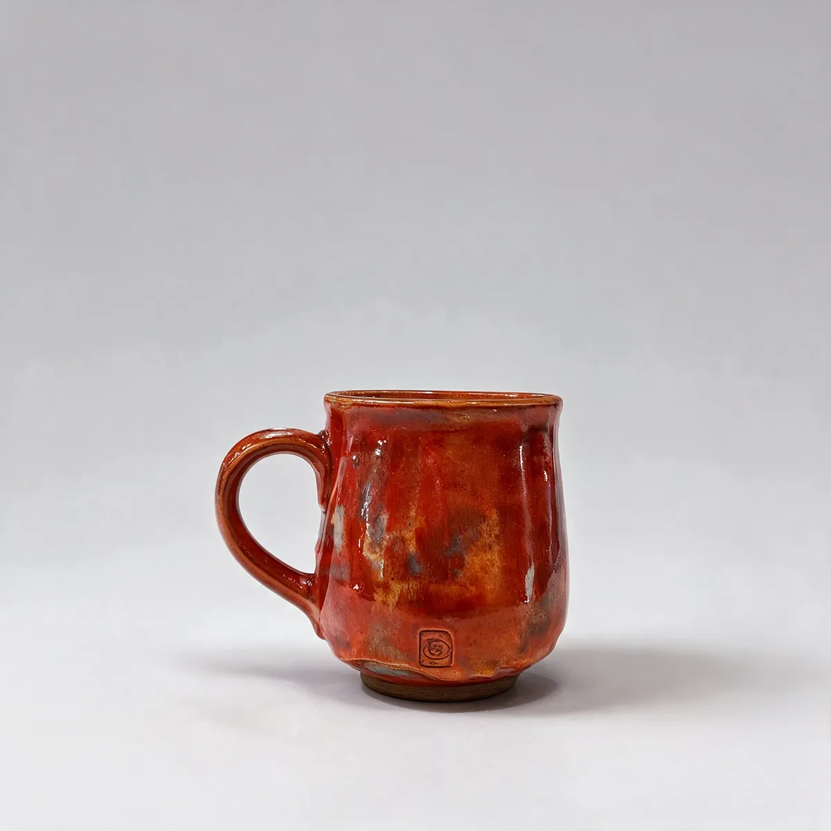 Czerwony ceramiczny kubek stoi na jasnoszarym tle.